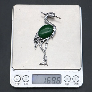 Detailed view of crane brooch with green gemstone on digital scale weighing 16.86g