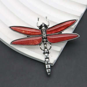 Close-up of vintage silver dragonfly brooch with red shell wings on a textured base