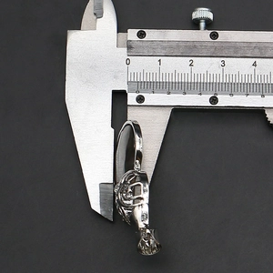 Measuring silver hollow metal pendant size with a caliper on a black background