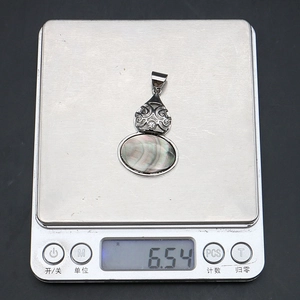 Detail showing natural abalone shell pendant on digital scale weighing 6.54 grams