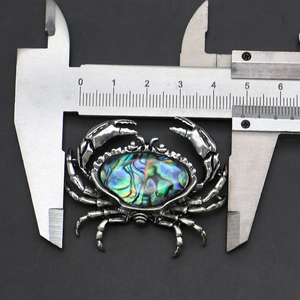 Detailed measurement of a crab brooch with abalone shell inlay using a metal caliper
