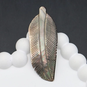 Macro detail of hand-carved feather shell pendant showing vibrant iridescent nacreous luster