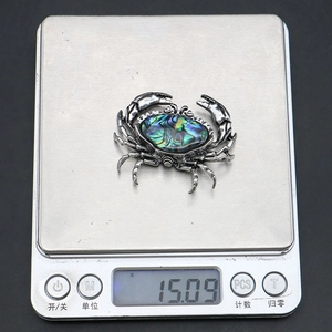 Detailed view of crab brooch featuring abalone shell inlay on an electronic digital scale