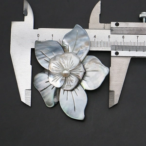 Macro shot of black shell flower pendant being measured with a metal caliper tool