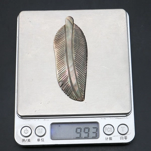 Detailed view of leaf-shaped iridescent shell pendant being weighed at 9.93 grams