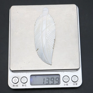 Macro shot of a white feather-shaped shell brooch weighing 13.99g on a digital scale