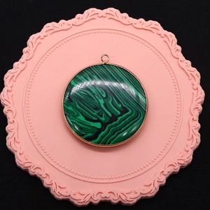 Macro detail of a round malachite pattern pendant with gold-plated metal edge framing