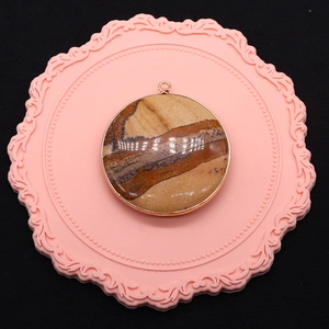Macro shot of circular picture stone pendant with golden plated edge on a pink lace mat