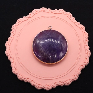Macro view of a circular purple amethyst pendant featuring a gold-plated metal border frame
