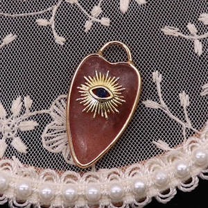 Macro shot of heart-shaped reddish stone pendant with golden evil eye and lace decor