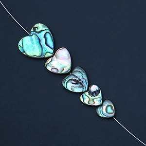 Dettaglio di cinque perle a cuore in conchiglia di abalone naturale con riflessi iridescenti