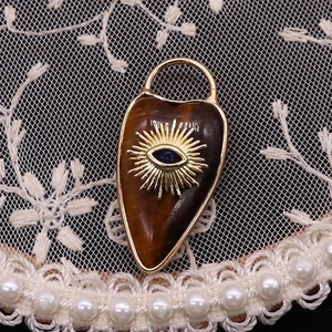 Macro shot of tiger eye stone heart pendant with gold evil eye inlay on lace background