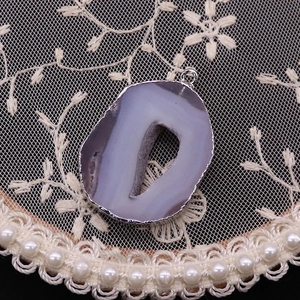 Close-up of natural purple agate slice pendant with silver plating and raw geode center