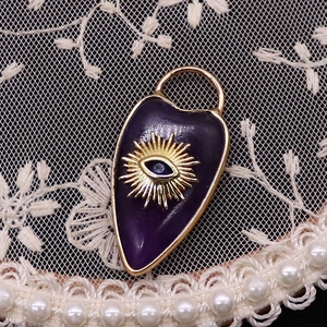 Macro shot of purple enamel heart pendant with golden evil eye on white lace