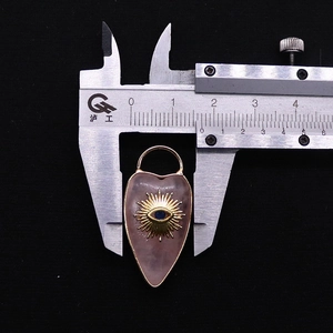 Macro shot measuring a pink quartz heart pendant with a golden sun evil eye motif