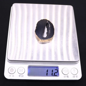 Detail van een zwarte agaat hanger van 11,2g met gouden rand op een digitale weegschaal