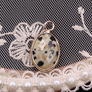 Macro shot of faceted dalmatian jasper oval pendant with gold edge on lace background