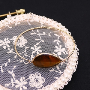Detalle de una piedra ojo de tigre ovalada en un brazalete dorado fino sobre encaje