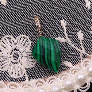 Macro d'un pendentif en malachite facettée avec bélière dorée et détails de dentelle