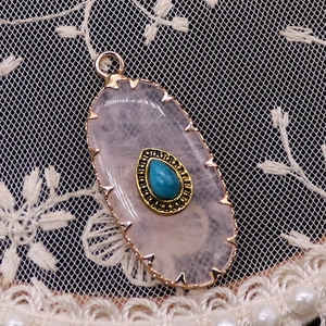 Macro shot of oval pink crystal pendant with blue turquoise inlay on white lace fabric