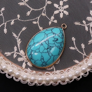 Detailed view of teardrop turquoise pendant with gold plated edge on lace and pearl decor