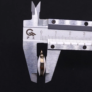 Caliper measuring the 8mm thickness of a shield-shaped natural stone pendant with gold edge