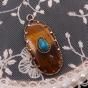 Detailed view of vintage oval pendant with turquoise inlay on gold metallic base