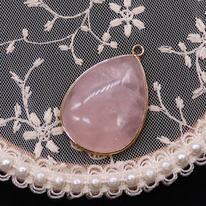 Close-up of teardrop rose quartz pendant with gold electroplated edges on lace fabric