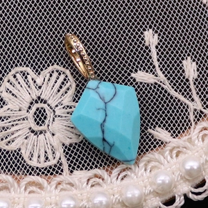 Vue macro d'un pendentif en turquoise avec bordure dorée sur fond de dentelle blanche