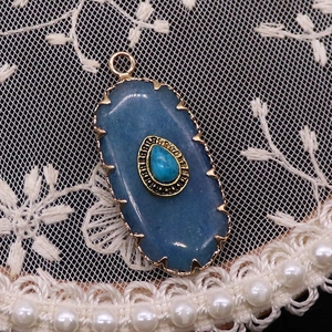 Macro shot of oval blue natural stone pendant with turquoise inlay and gold relief frame