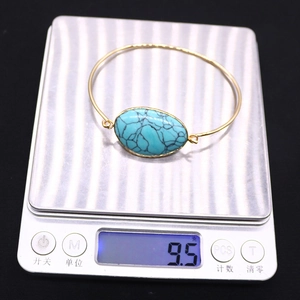 Adjustable gold-finish bangle with oval turquoise stone weighing 9.5 grams on a digital scale