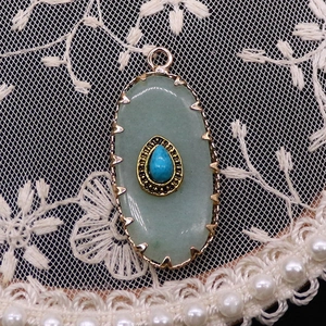 Macro detail of oval green aventurine pendant with blue turquoise inlay and golden frame
