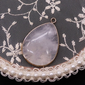 Macro shot of a teardrop rose quartz pendant with gold metal frame on white lace