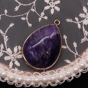 Macro shot of purple teardrop stone pendant with gold plating and natural crystal texture