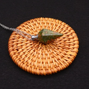 Detailed macro of unakite crystal perfume bottle pendant with silver chain on woven mat
