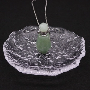 Détail macro du pendentif flacon d'huile en aventurine verte sur un plat en verre