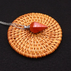 Close-up of red jasper hexagonal column perfume bottle pendant with silver chain on rattan mat