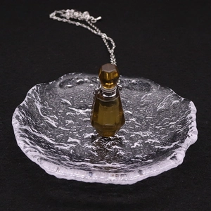 Détail d'un collier flacon d'huile essentielle en verre fumé sur un plateau en verre