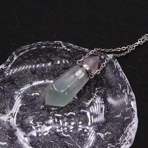 Close-up of a green crystal perfume bottle pendant with a pink tip and silver chain
