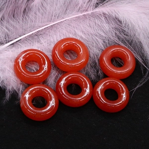 Dettaglio di sei perle donut in agata rossa lucida su piume rosa e sfondo nero elegante