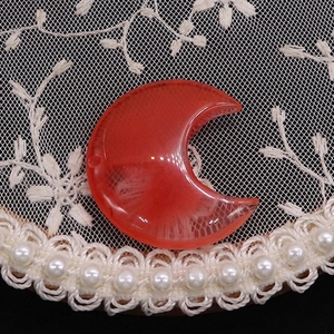 Macro shot of red crescent moon pendant with white texture on white lace background