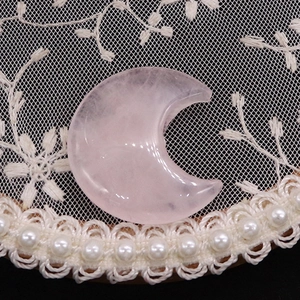 Close-up of crescent-shaped natural rose quartz stone on white lace embroidery with pearls