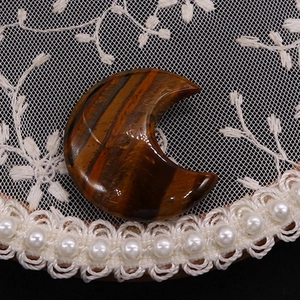 Detailed macro shot of polished crescent moon tiger eye stone on elegant lace background