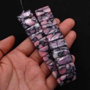 Detail von handgehaltenen rechteckigen rosa und schwarz gefleckten Natursteinperlen für DIY