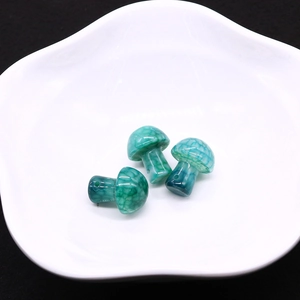 Macro shot of three mushroom-shaped green dragon vein agate beads on a white plate