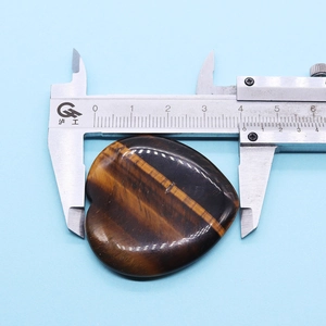 Medición de piedra ojo de tigre corazón de 40mm con un calibrador en fondo azul