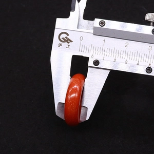 Close-up showing a vernier caliper measuring the width of a polished red agate ring