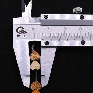 Macro detail of natural stone heart beads being measured by a caliper tool