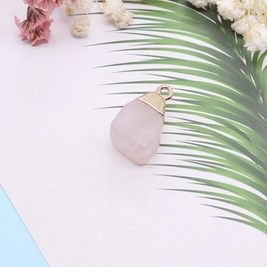 Detail shot of natural raw rose quartz pendant with gold electroplated rim on a palm leaf