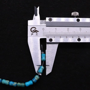 Gros plan mesurant une perle de turquoise en forme d'os de 8mm avec un étrier